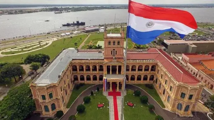 Imagen aérea del Palacio Lopez en Asunción con la bandera paraguaya y el río Paraguay de fondo